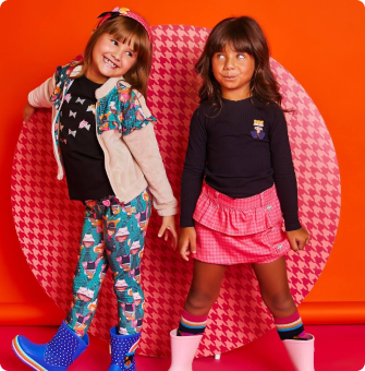 Meninas sorridentes com roupas coloridas e fundo laranja vibrante.